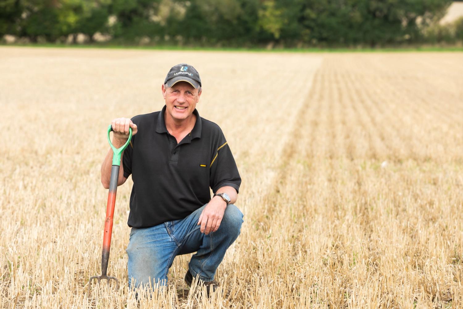 Farmer David Miller crouching down in field, holding a spade
