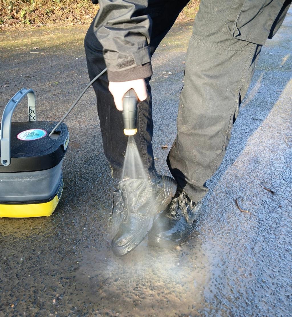 Person washing boots with a spray hose and disinfectant
