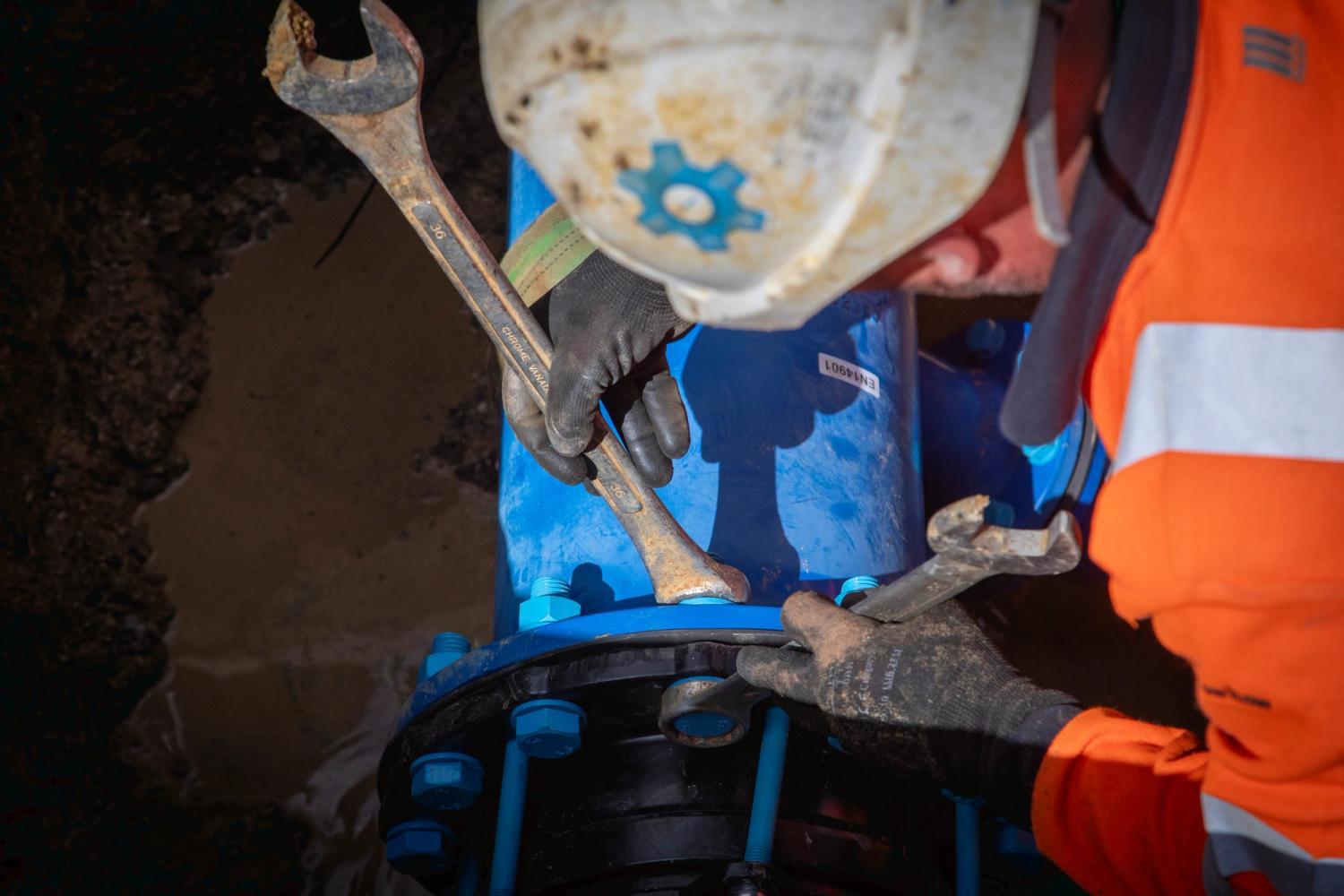 Image shows a man in protective clothing installing a water main