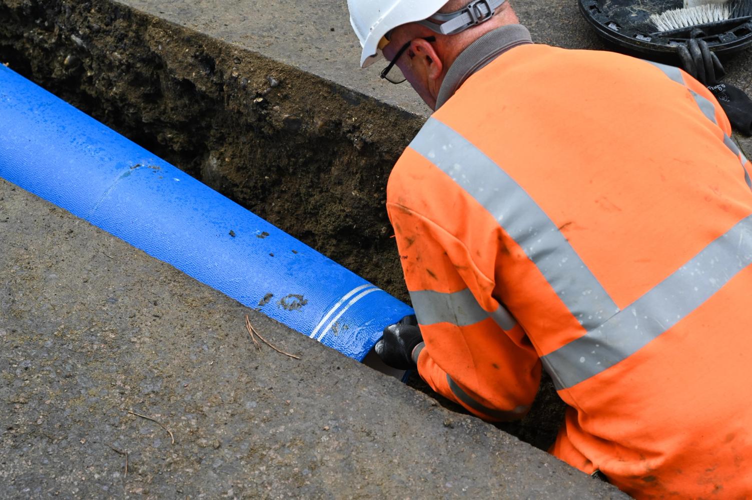 A pipe is put into position in the ground by a man in high-visibility clothing