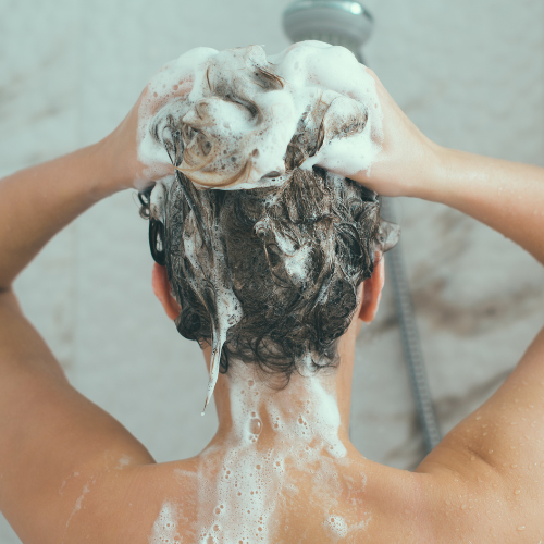 An image of a woman's hands lathering shampoo in her hair while showering.