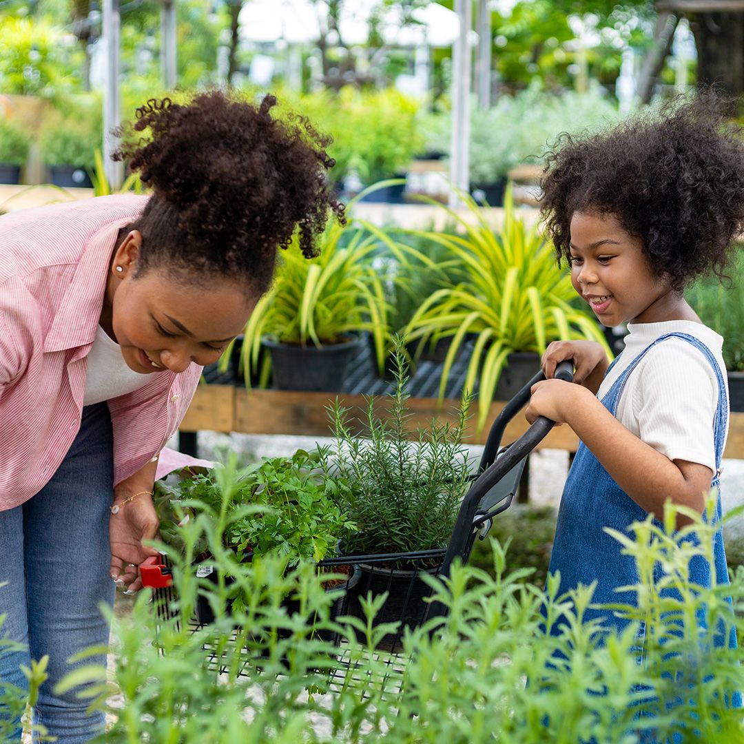 Mother and daughter watering plants in a greenhouse with a watering can