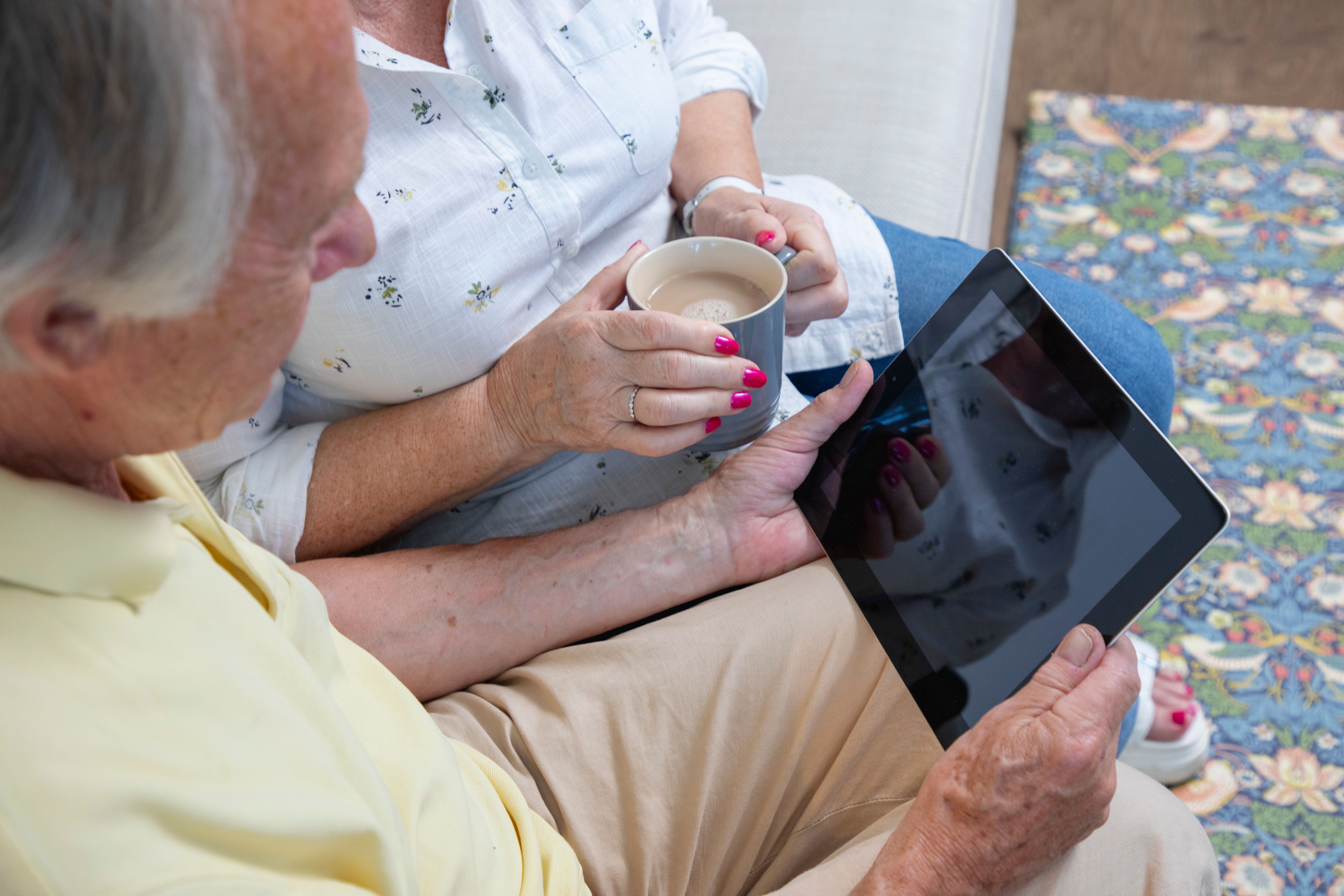 an elderly couple sat on a sofa looking at an ipad 