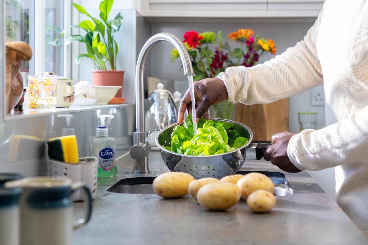 Man washing vegetables and salad in a strainer at the sink