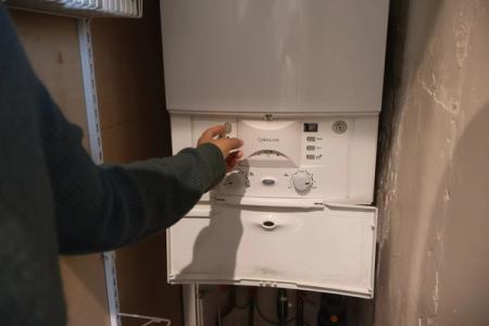 A man is switching off the water supply at the boiler.