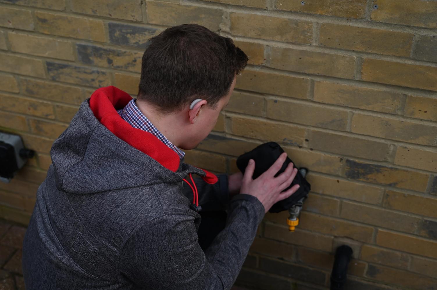 A man protecting an outside tap with a tap jacket in winter