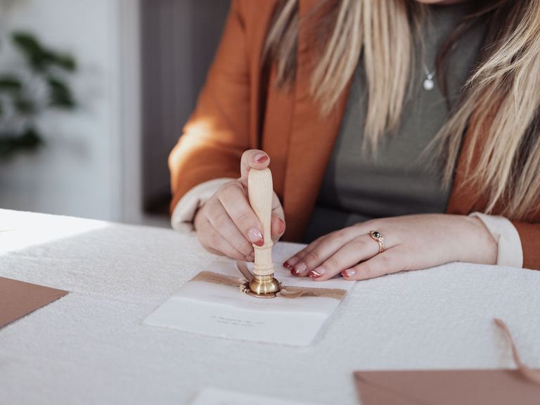 A pair of hands stamping sealing wax onto a wedding invitation