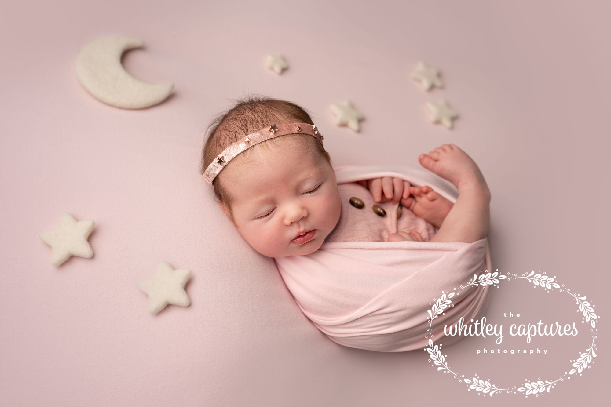 Sleeping newborn wrapped in pink, surrounded by little stars