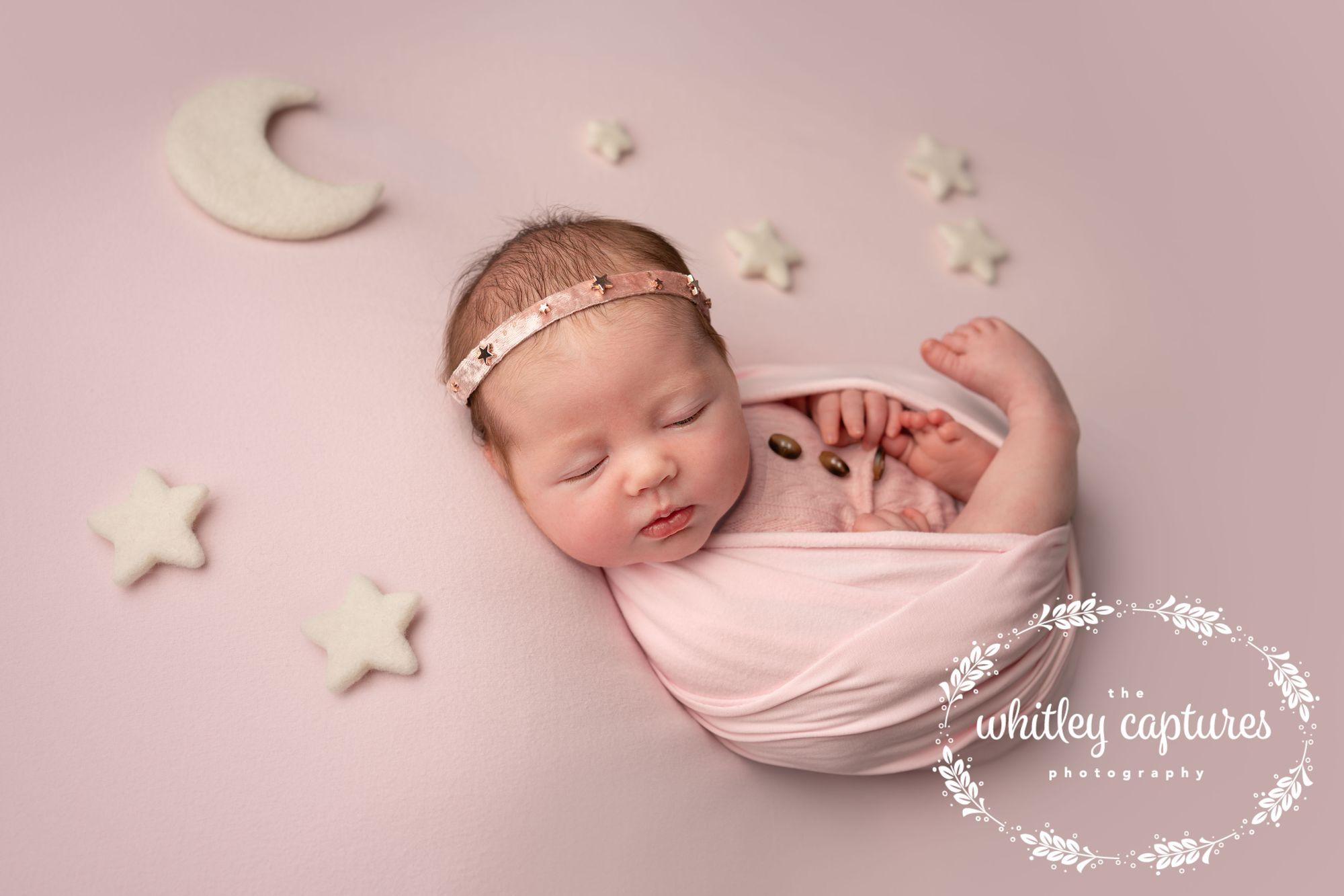 Sleeping newborn wrapped in pink, surrounded by little stars