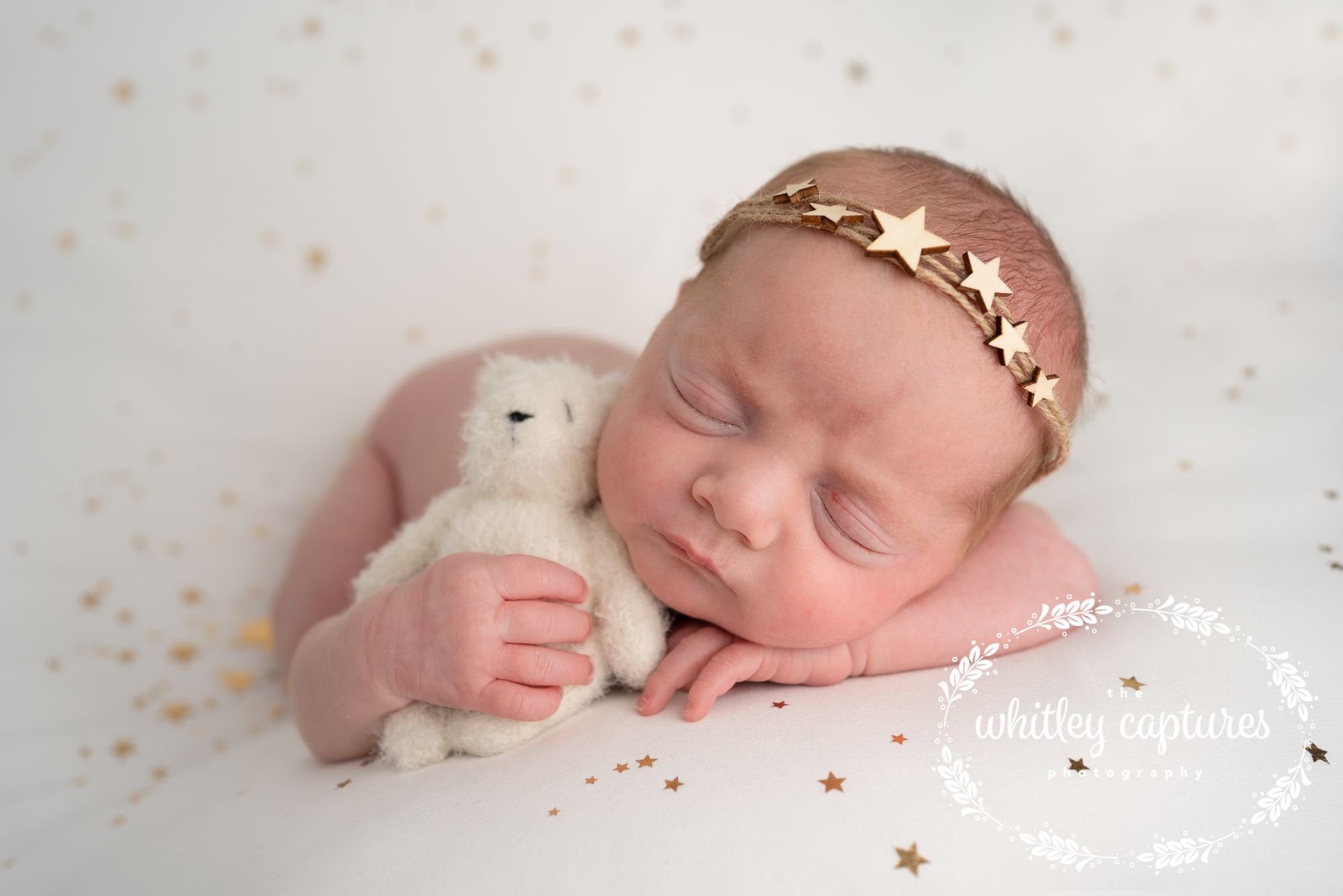 Sleeping baby wearing a star headband and cuddling a soft toy