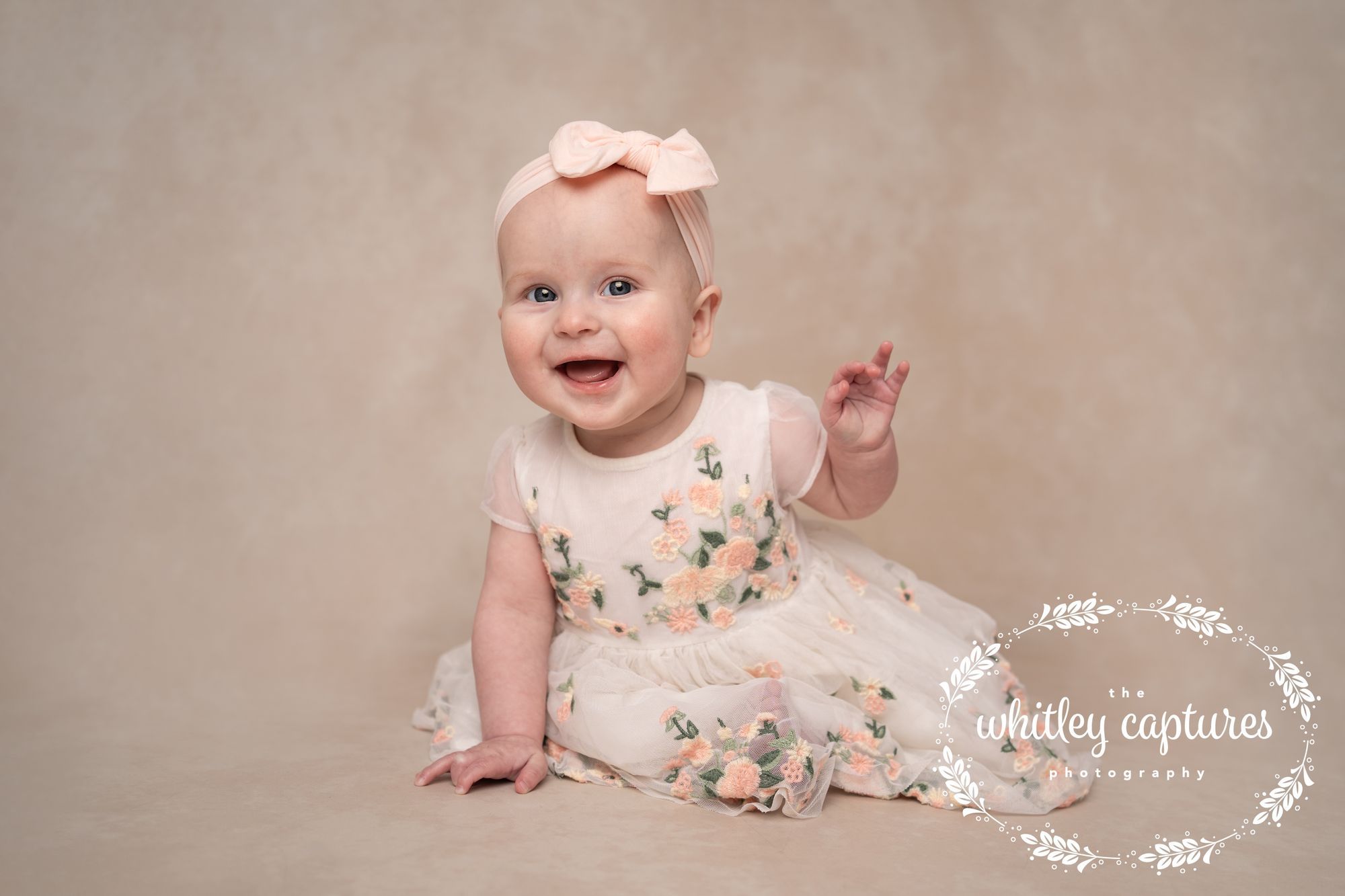A smiling baby sitting in a floral dress