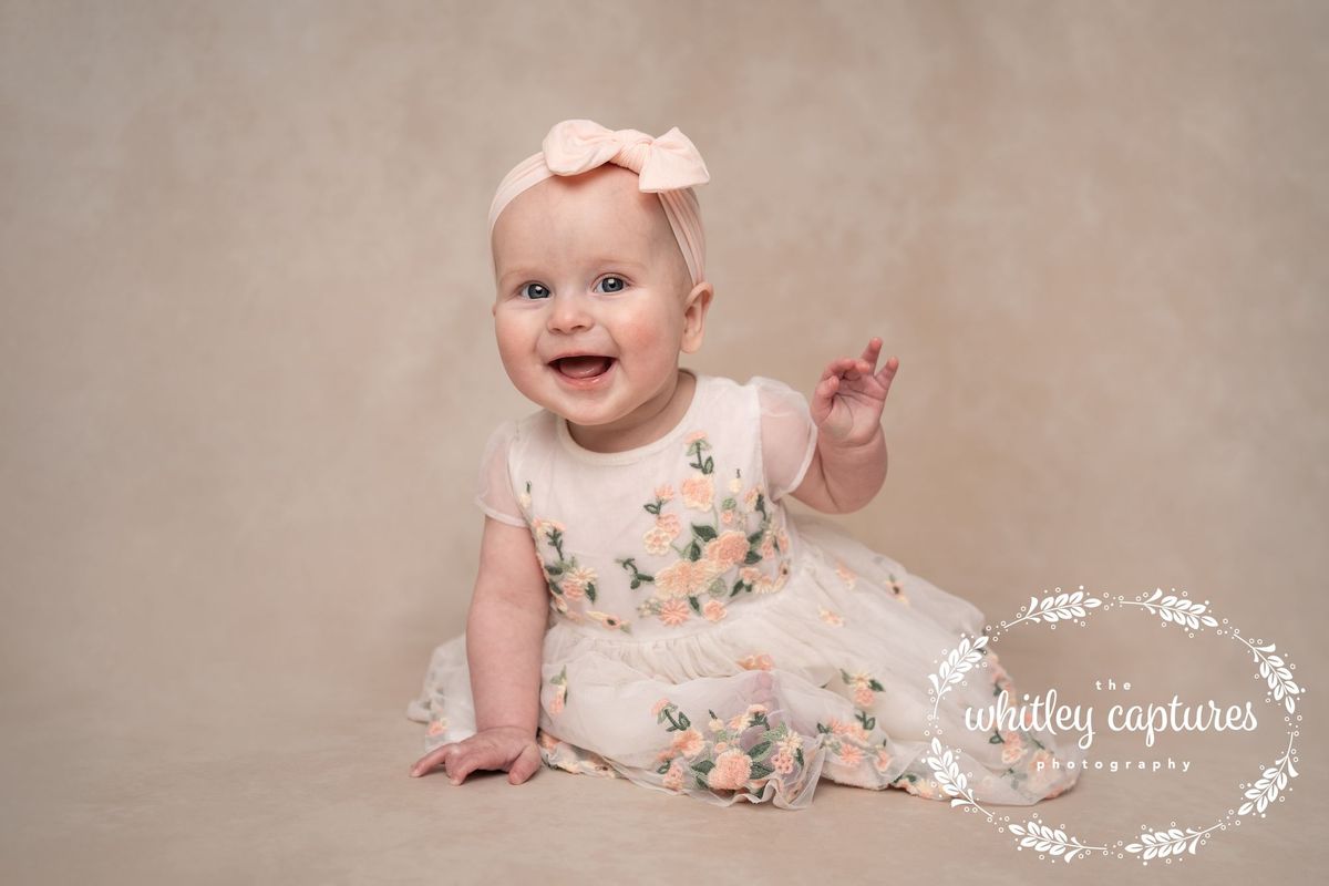 A smiling baby sitting in a floral dress