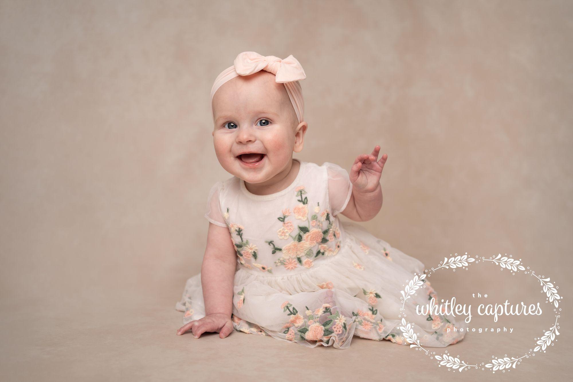 A smiling baby sitting in a floral dress