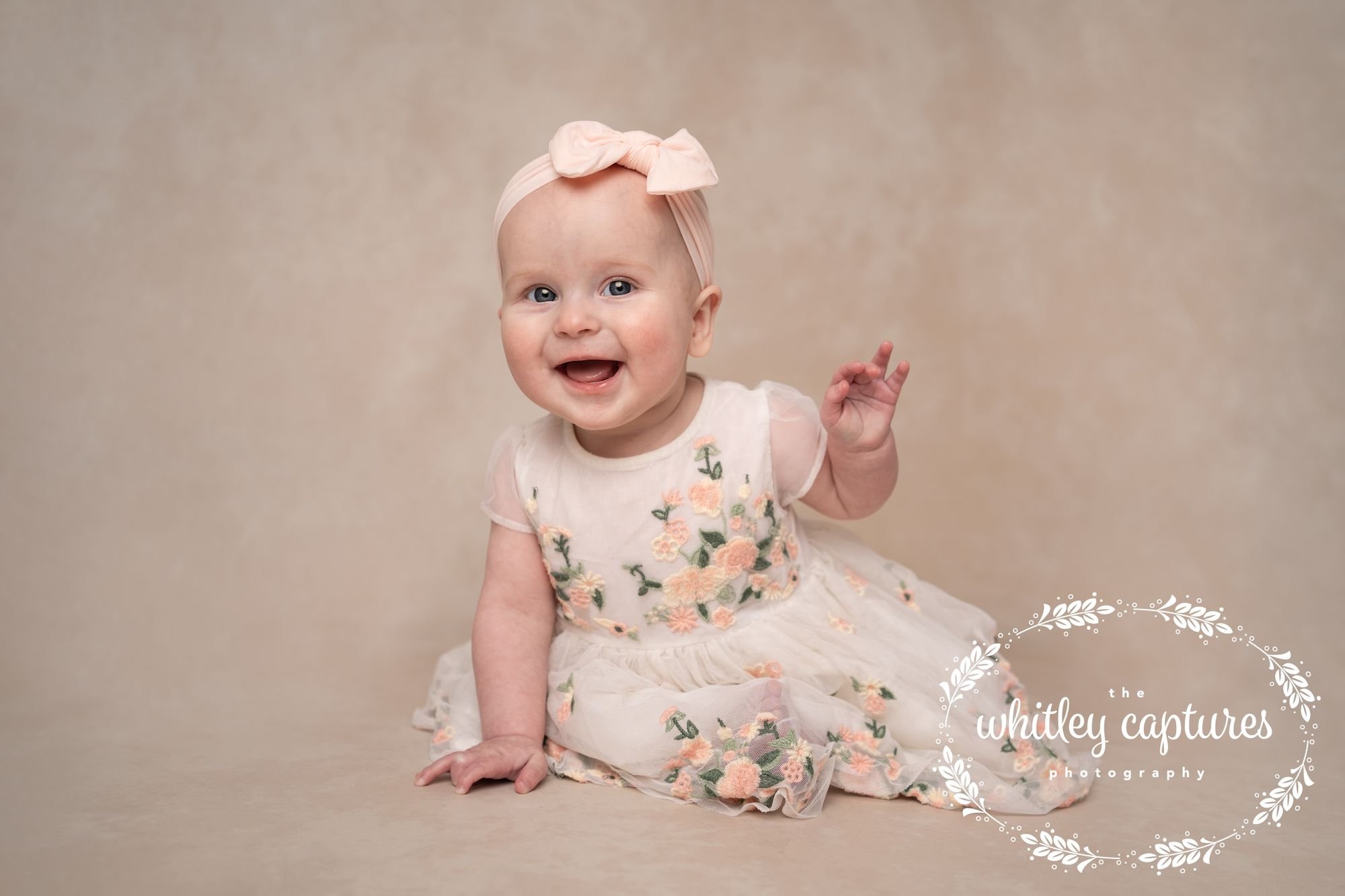 A smiling baby sitting in a floral dress