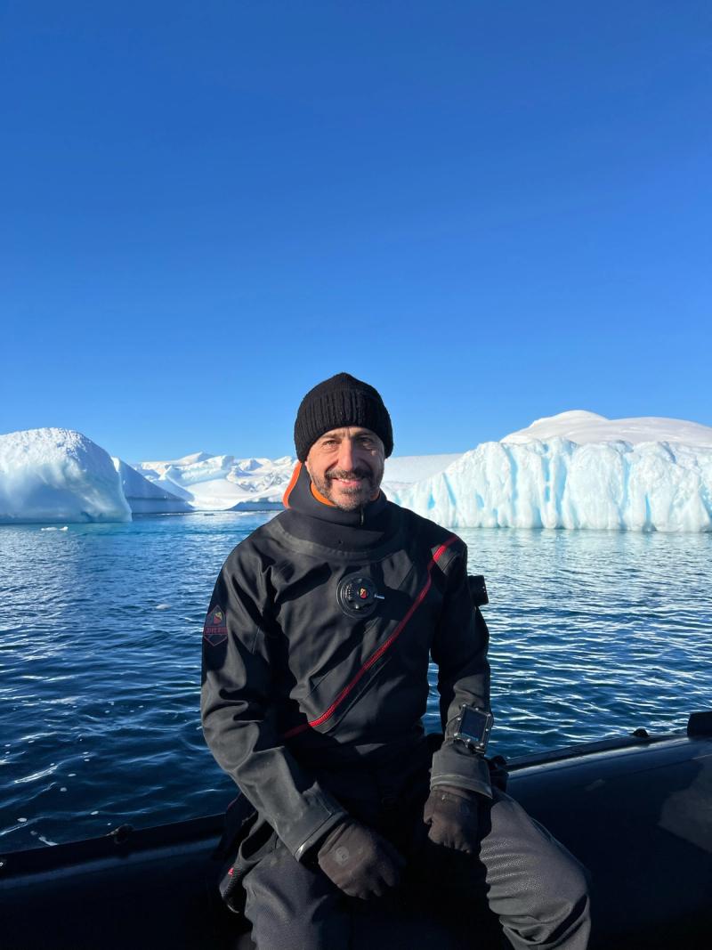 Luis, buzo de 65 años con gorro sentado frente a un glaciar
