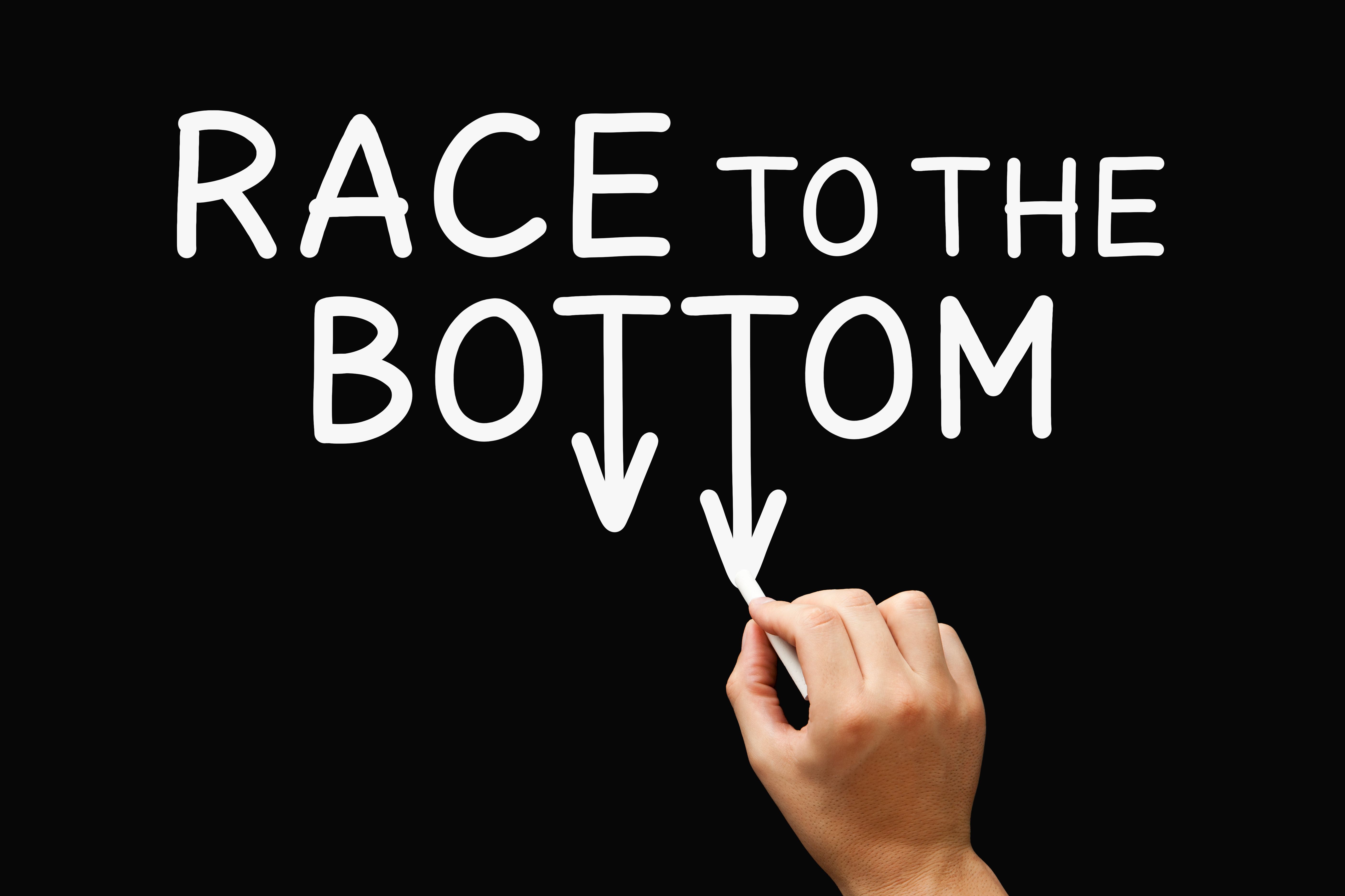 The words "RACE TO THE BOTTOM" in white on a black background, with downward arrows and a hand drawing them, illustrating a declining trend.