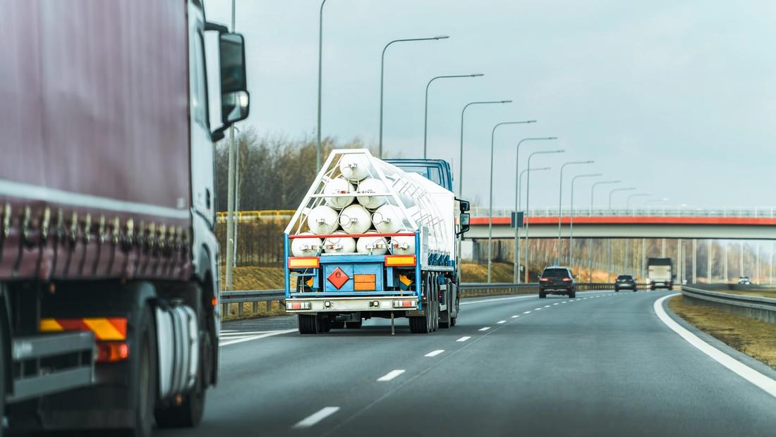 A transport truck displaying orange and red dangerous goods placards on its trailer