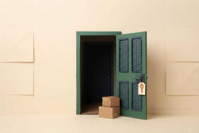Paper-craft illustration of a folded kraft-paper apartment door with a small paper key ring hanging from the lock and a paper wall calendar beside it