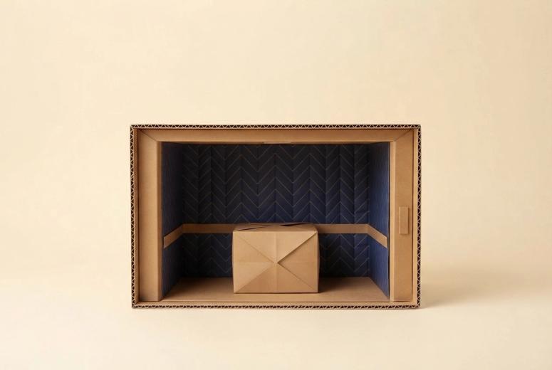 Paper-craft illustration of a folded-paper elevator car with quilted paper pads hung inside, doors held open, and a small kraft paper box waiting in the corridor