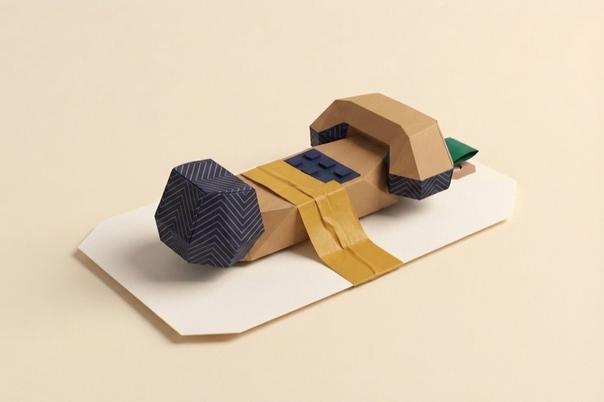 Paper-craft illustration of a folded-paper telephone handset on a gummed paper label with amber tape