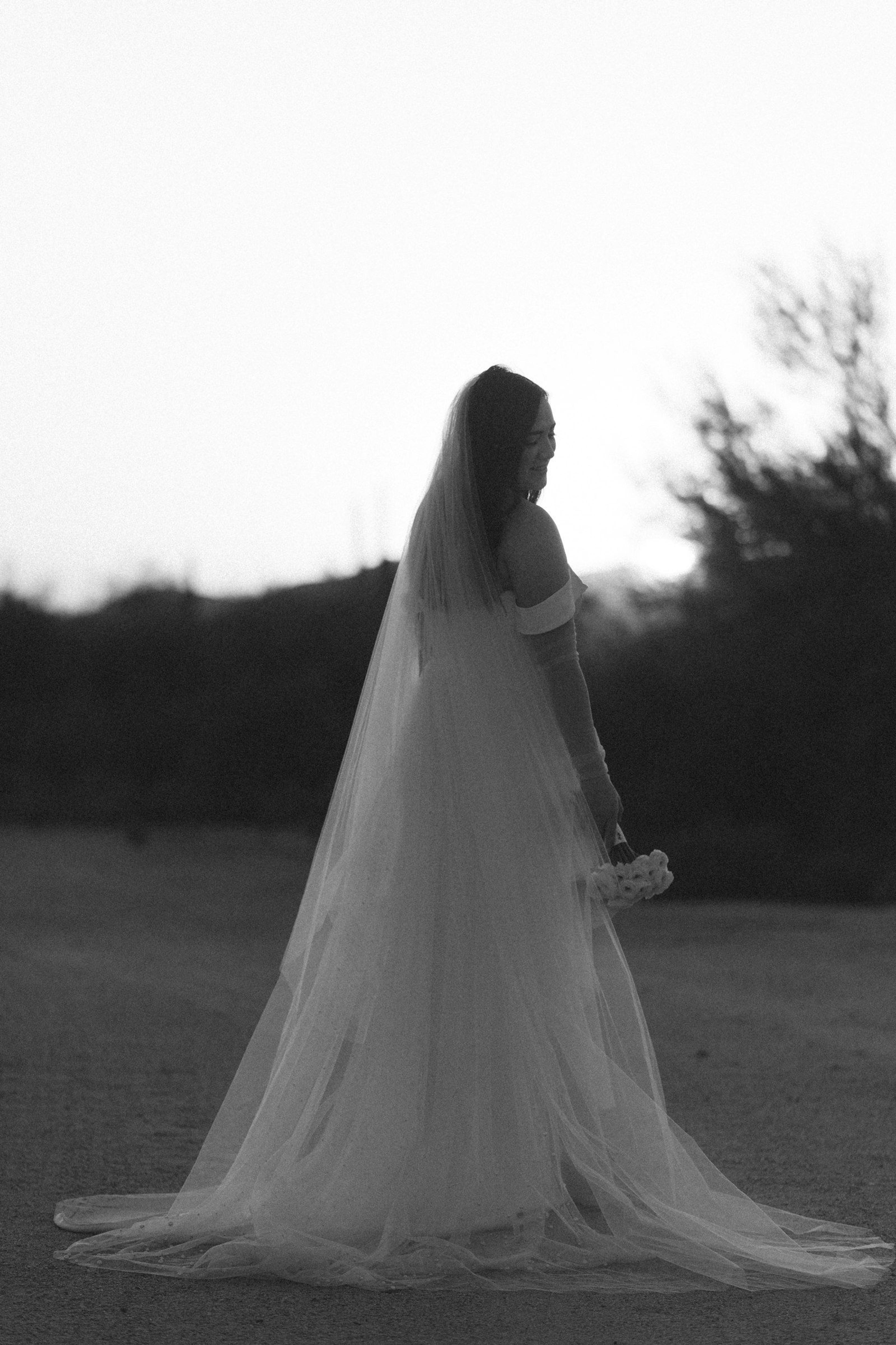 A bride in a flowing dress holding a bouquet outdoors in warm relaxed light
