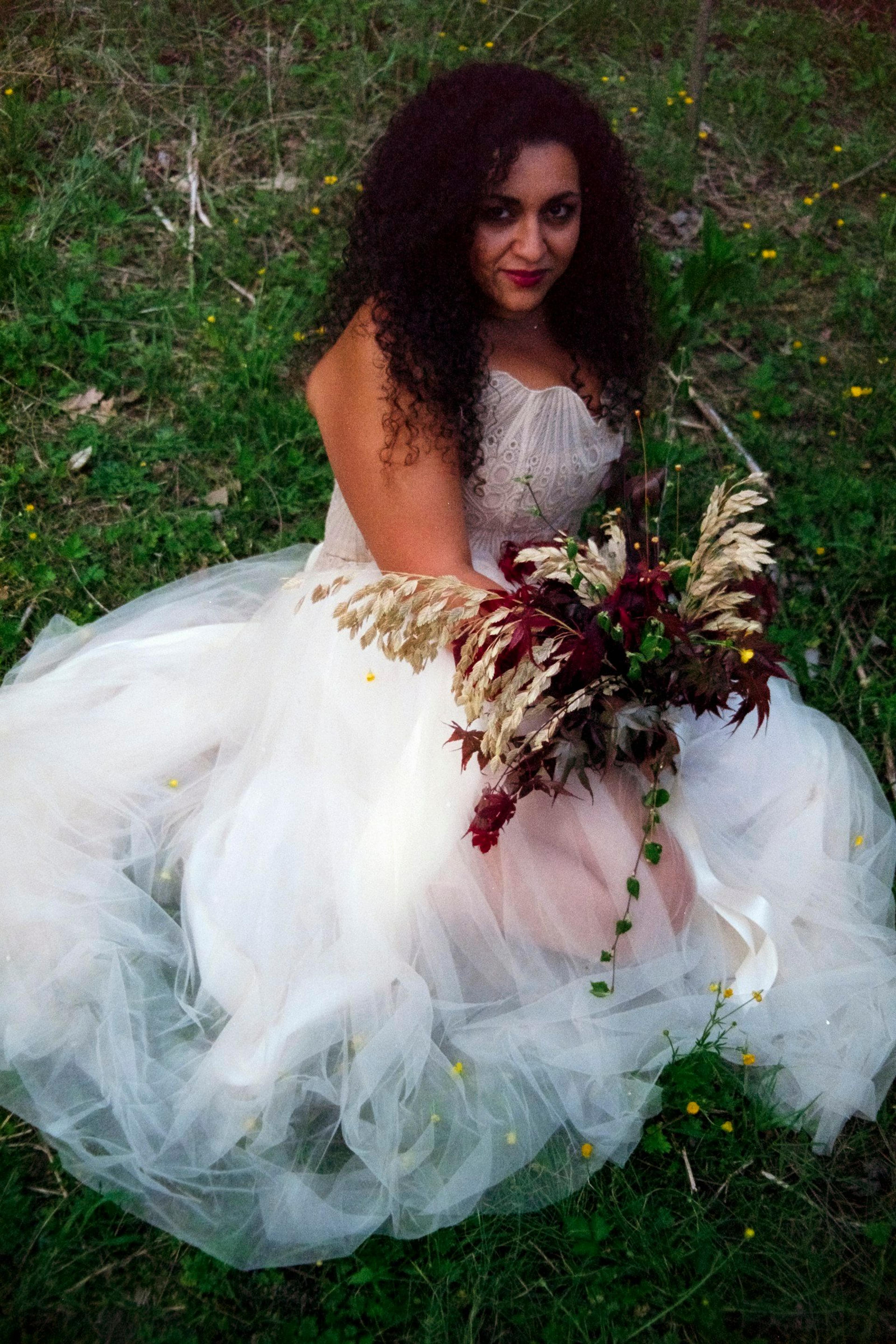 A bride in a relaxed white dress holding a bouquet outdoors in soft natural light