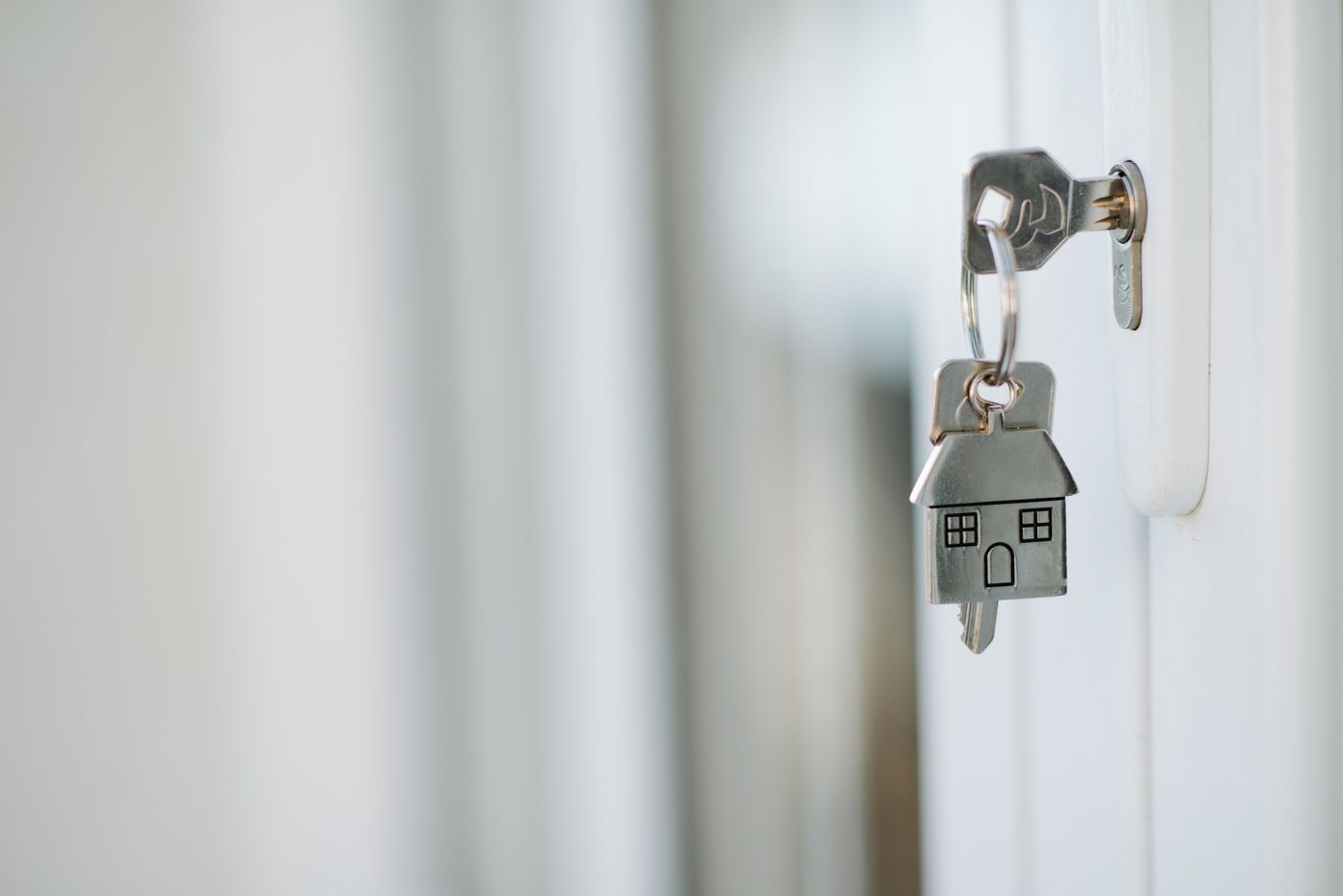 House key inserted in a clean residential front door lock with a house-shaped keychain, symbolizing youth independence and housing stability