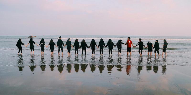 Gruppe steht Hand in Hand im flachen Wasser am Strand
