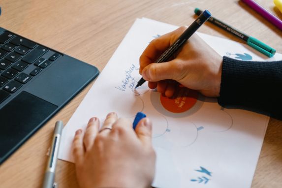 Hand zeichnet mit Stift ein Diagramm auf Papier neben einem Tablet mit Tastatur