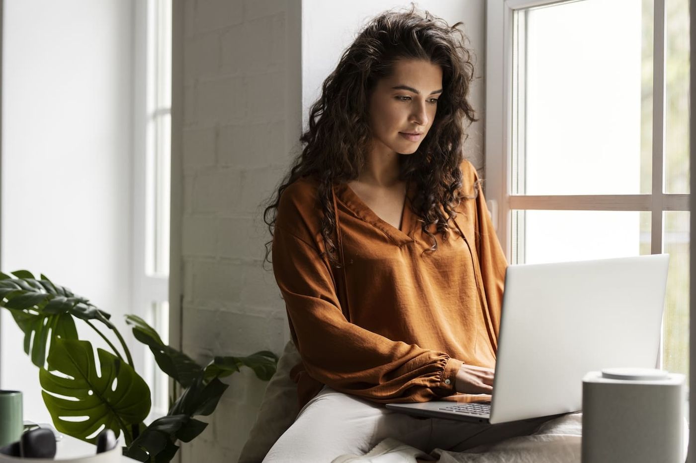 Frau sitzt am Fenster und arbeitet konzentriert am Laptop