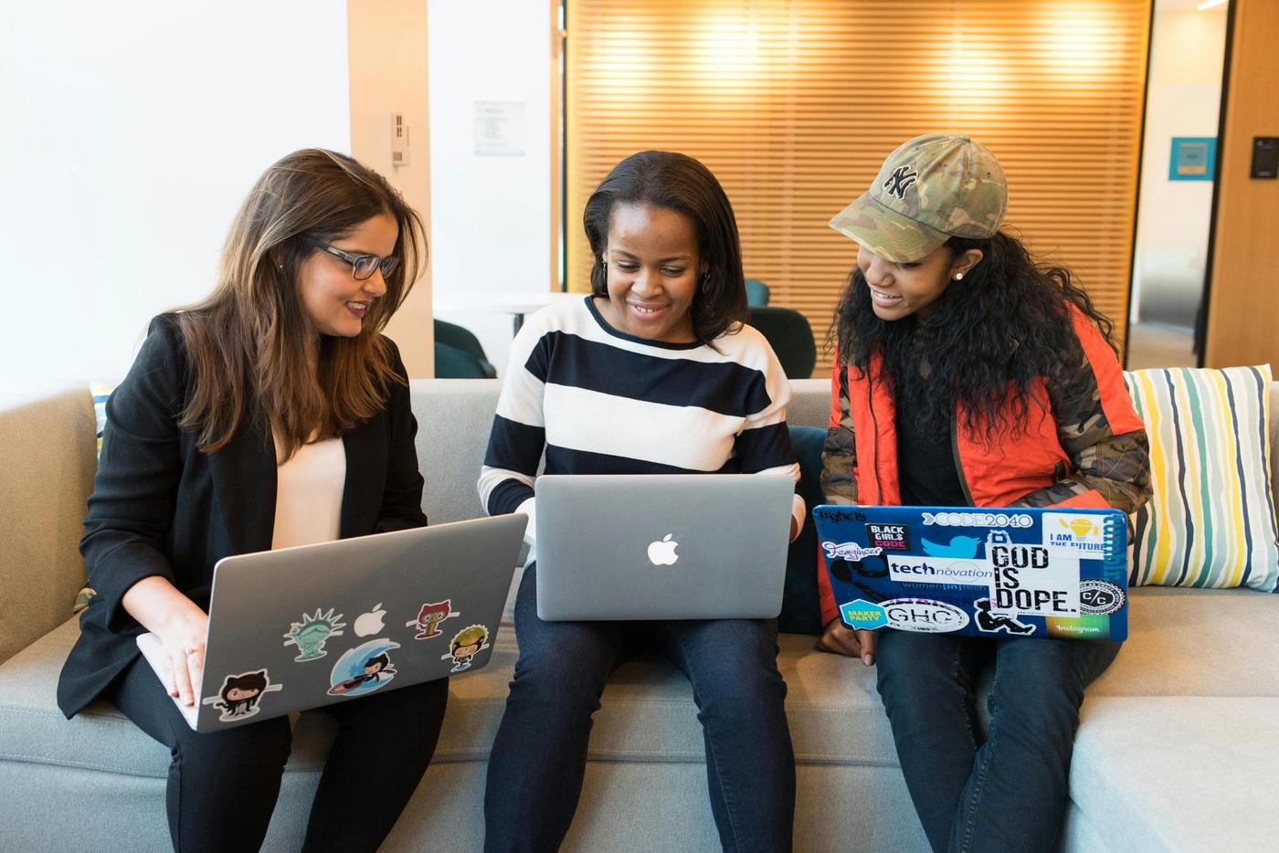 Drei Frauen sitzen nebeneinander auf einem Sofa und arbeiten an Laptops