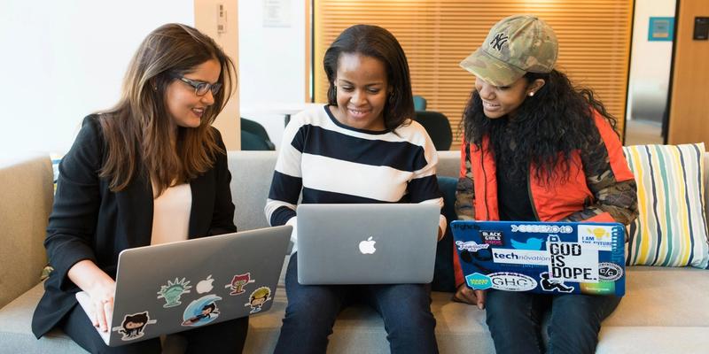 Drei Frauen sitzen nebeneinander auf einem Sofa und arbeiten an Laptops
