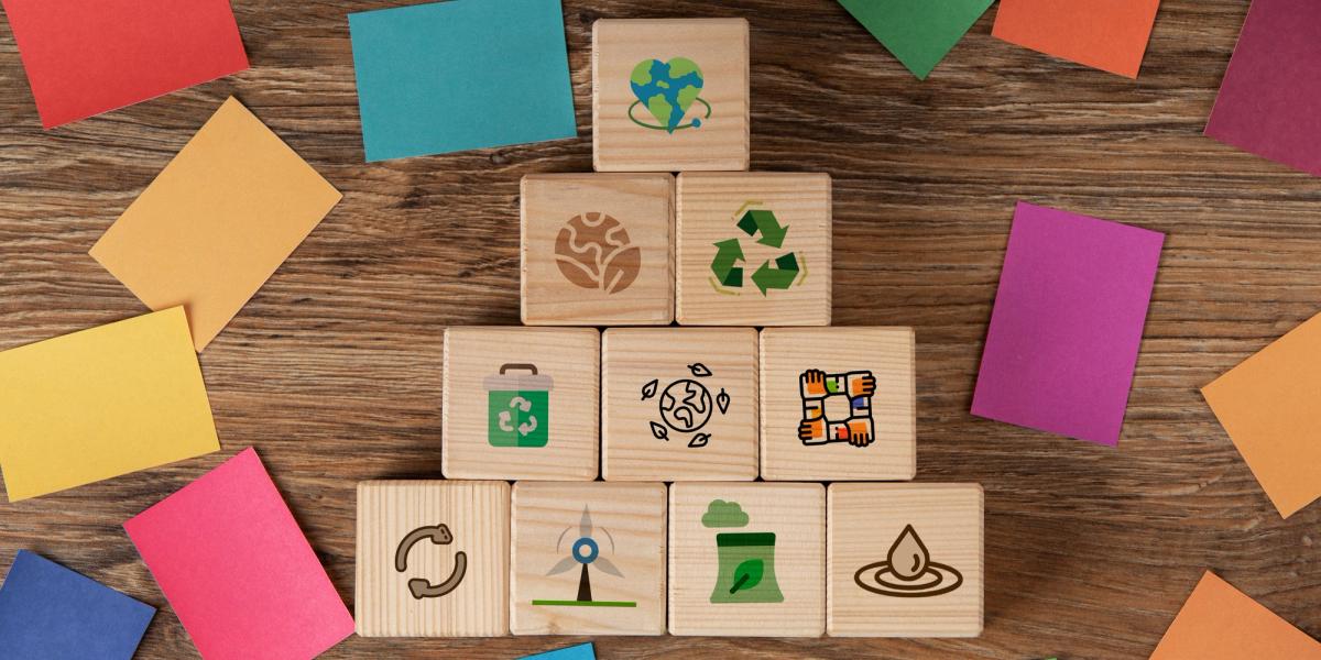 A pyramid of wooden blocks with environmental symbols, surrounded by colorful paper cards on a wooden surface.