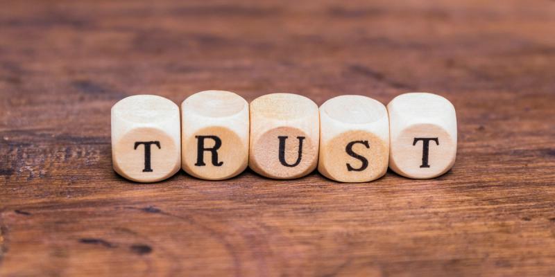 Holzwürfel mit Buchstaben bilden das Wort „TRUST“ auf einem Holztisch