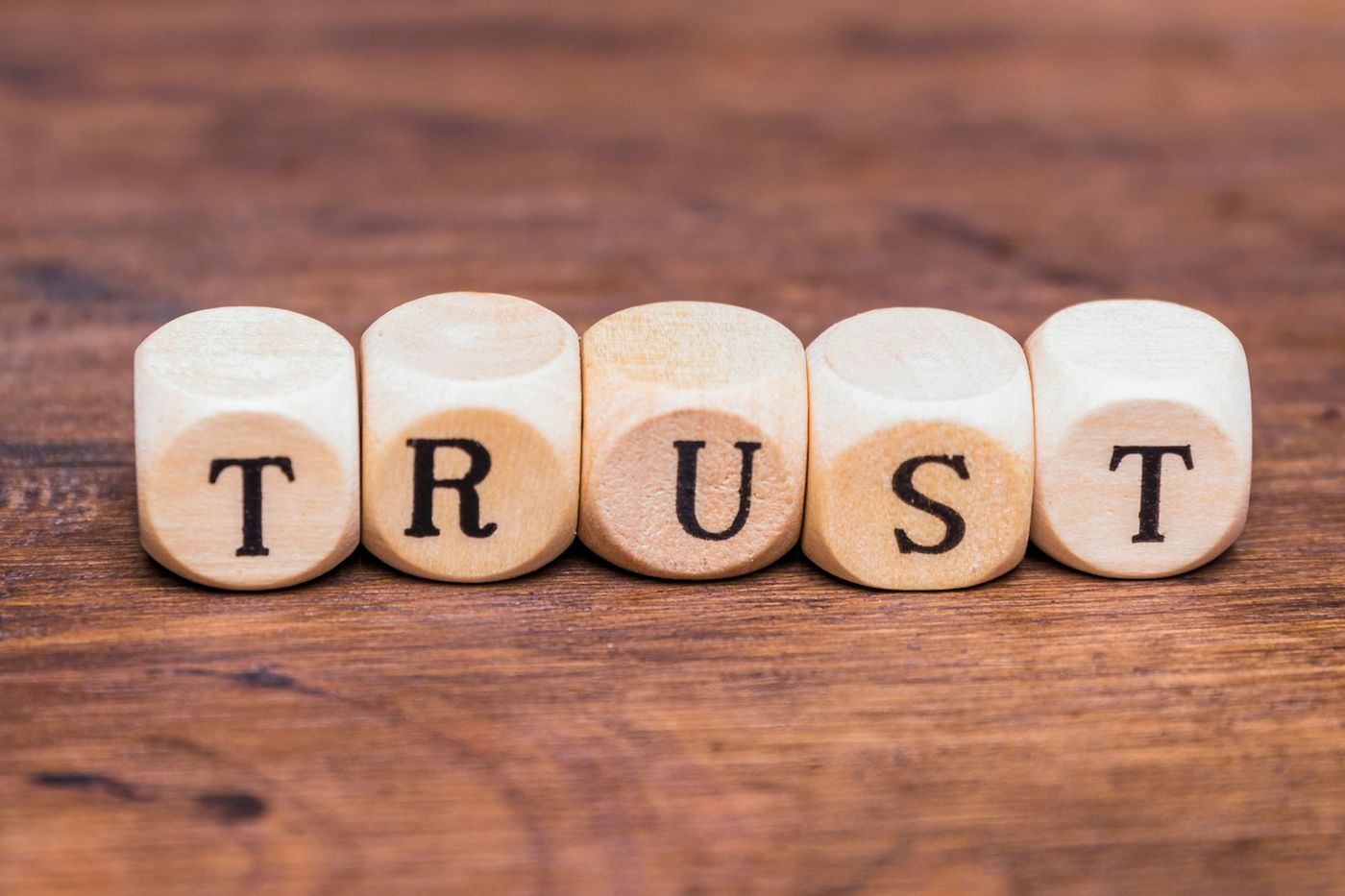 Holzwürfel mit Buchstaben bilden das Wort „TRUST“ auf einem Holztisch