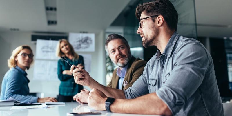 Team bespricht sich an einem Konferenztisch, ein Kollege erläutert seine Punkte