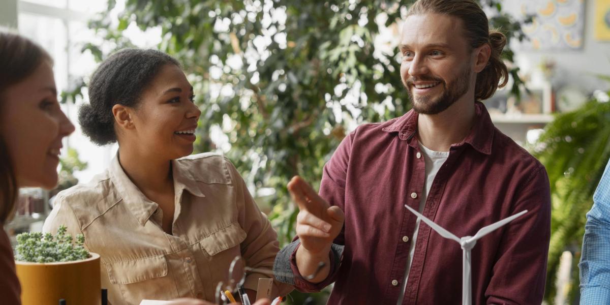 A group of four people engaged in a lively discussion, surrounded by plants and a small wind turbine model.