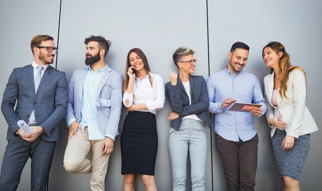 Gut gelauntes Team in Businesskleidung steht nebeneinander an einer Wand