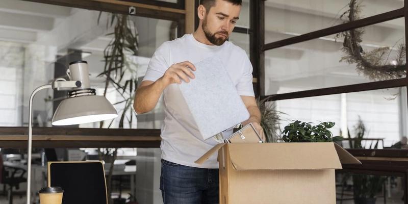 Mann packt am Schreibtisch persönliche Sachen in einen Umzugskarton