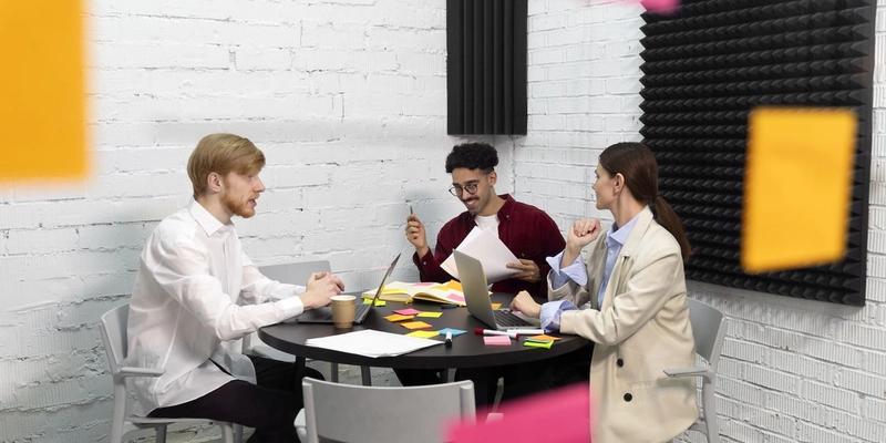 Drei Kollegen besprechen sich am Tisch mit Laptops und bunten Haftnotizen