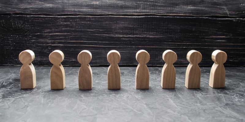 Acht Holzfiguren stehen in einer Reihe vor dunklem Holzhintergrund