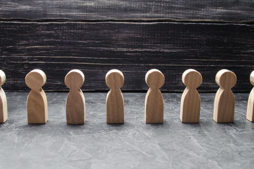 Acht Holzfiguren stehen in einer Reihe vor dunklem Holzhintergrund