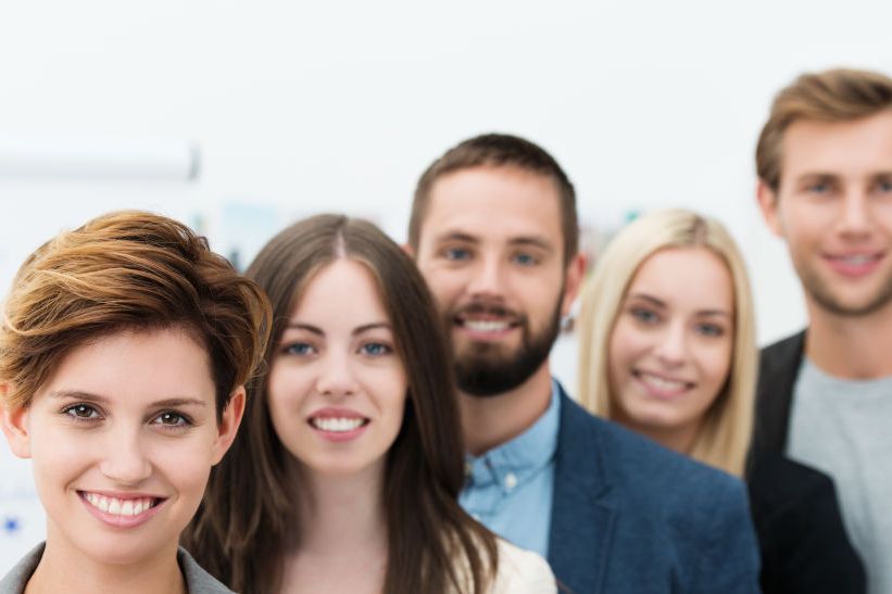 Gruppe lächelnder Kolleginnen und Kollegen steht hintereinander in einem Büro