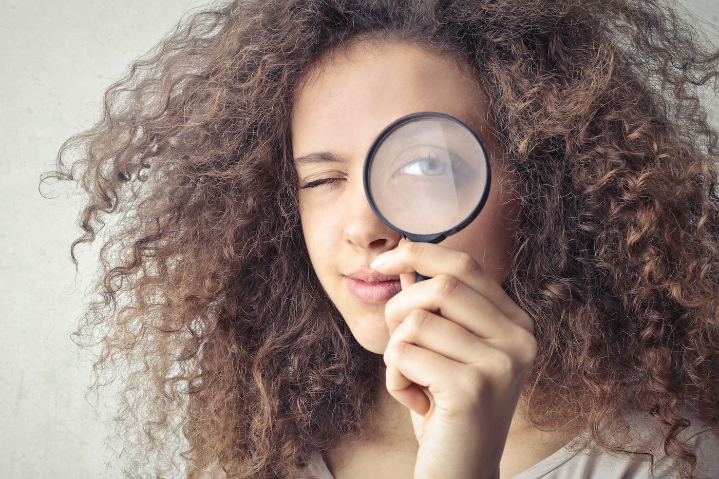 Frau blickt mit einem Auge durch eine Lupe