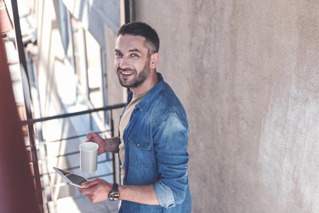 Lächelnder Mann mit Kaffeetasse und Tablet auf einem Balkon