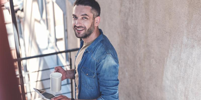 Lächelnder Mann mit Kaffeetasse und Tablet auf einem Balkon