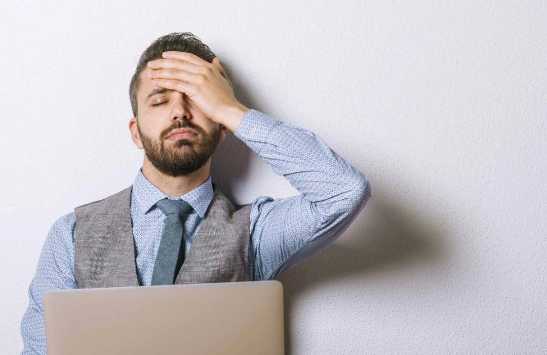 Gestresster Mann mit Hand an der Stirn hinter einem Laptop