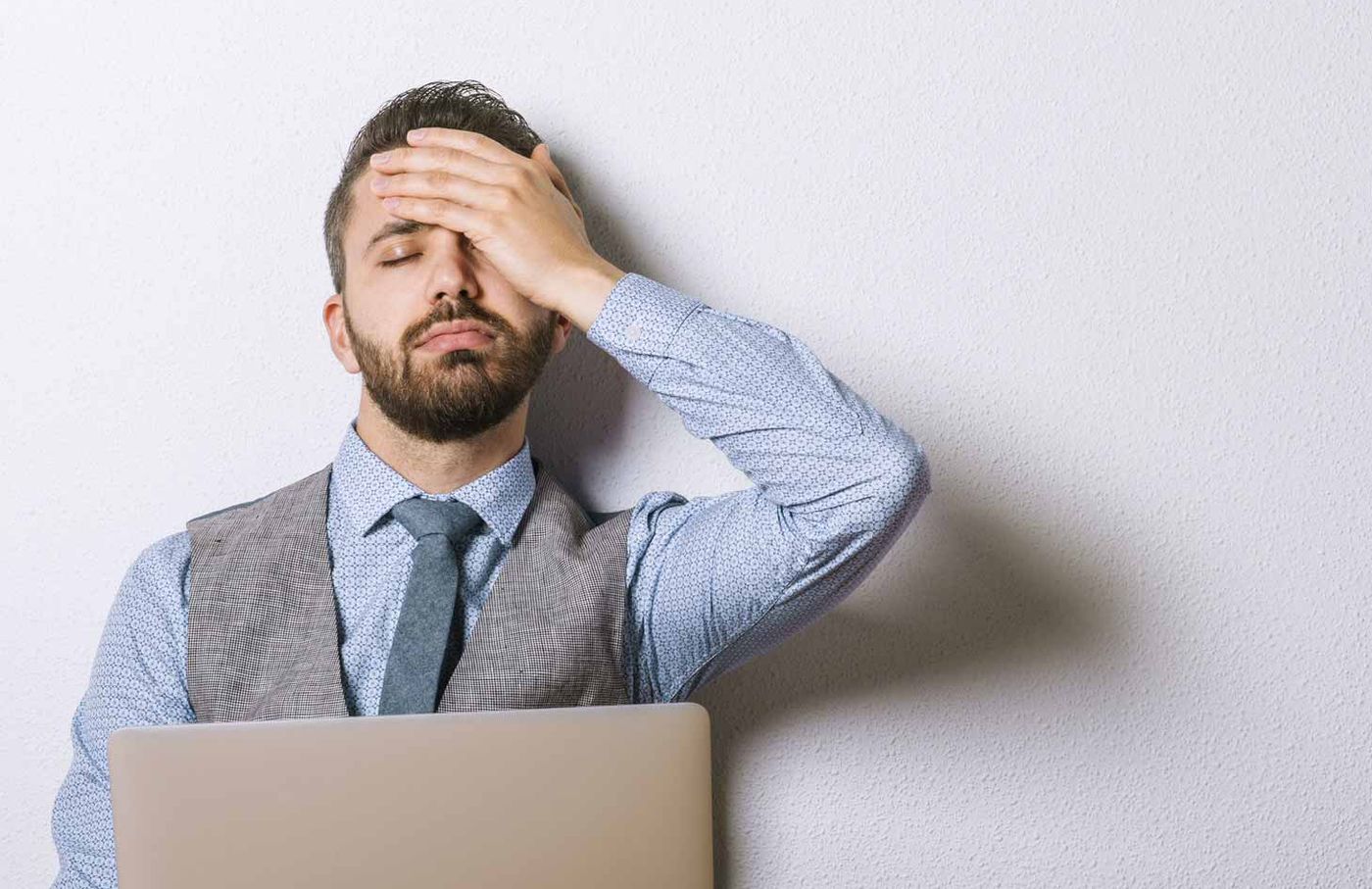 Gestresster Mann mit Hand an der Stirn hinter einem Laptop