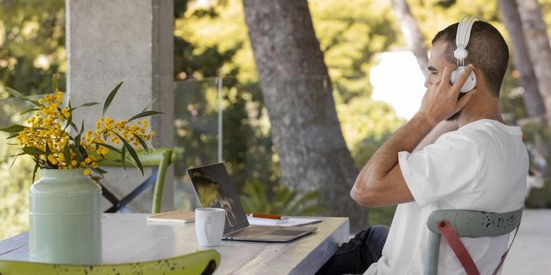 Mann mit Kopfhörern arbeitet am Laptop an einem Tisch im Freien
