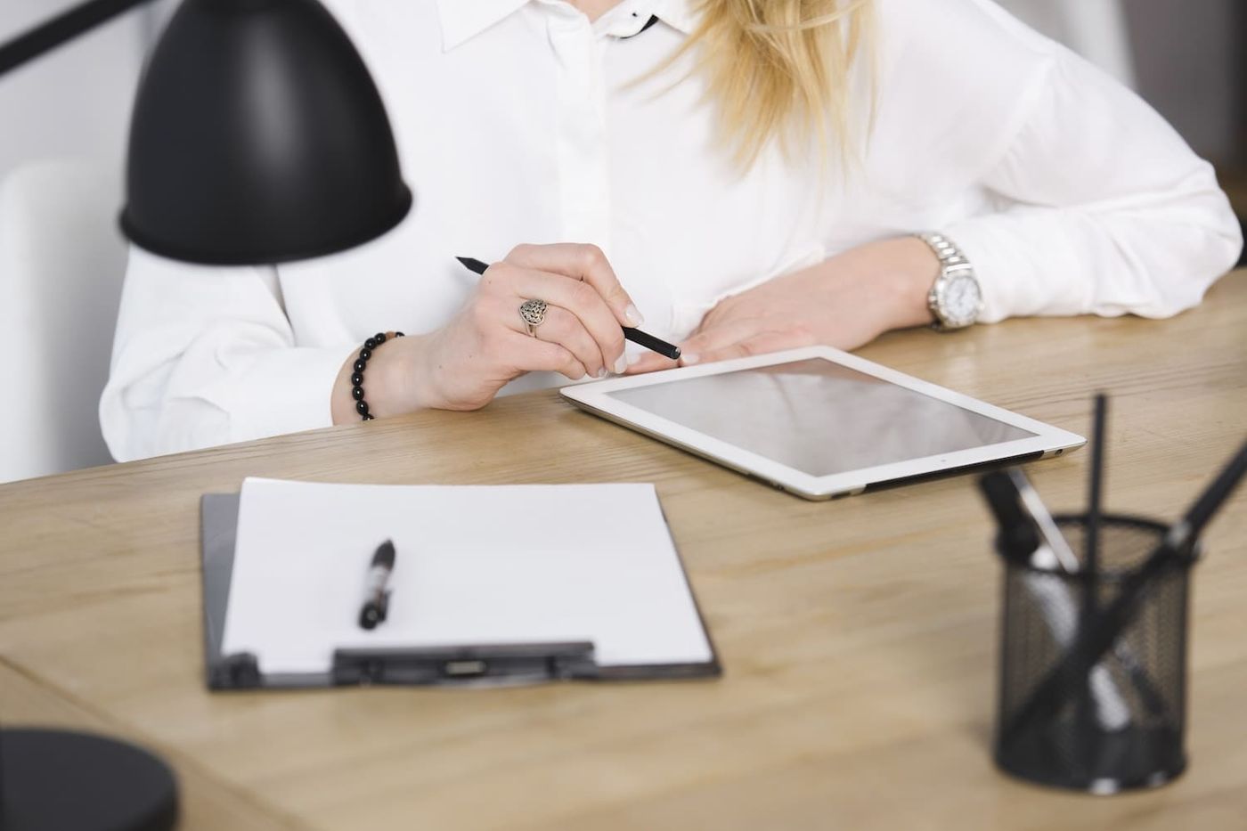 Person mit Stift am Schreibtisch vor Tablet und Klemmbrett mit leerem Dokument